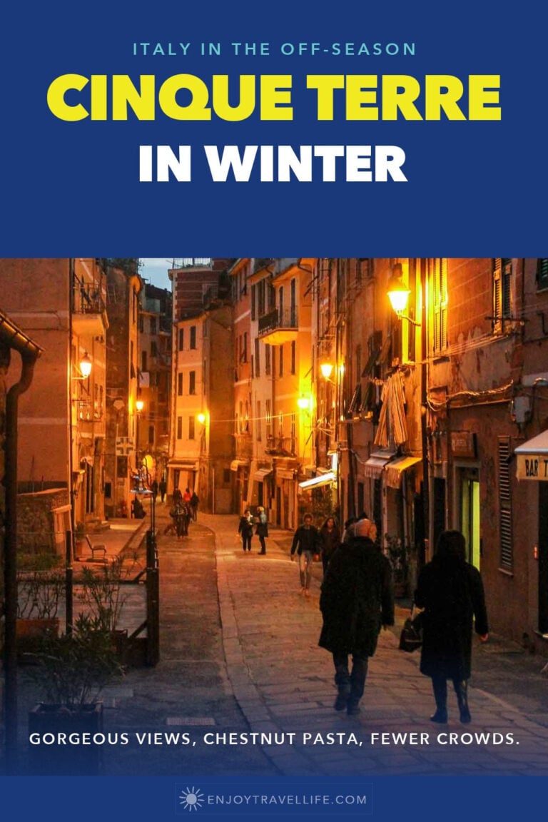 A lamplit street in Vernazza, Cinque Terre, on a winter evening with a few people walking.