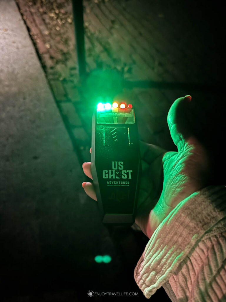 A handheld EMF meter glows green in the dark during the evening walk.