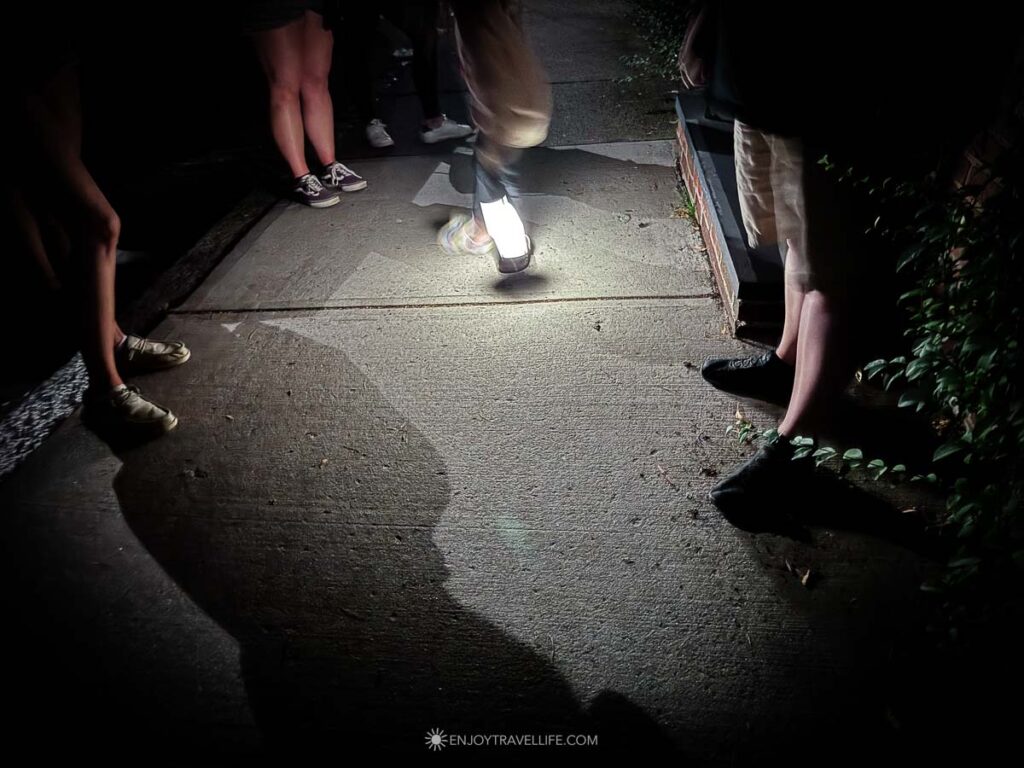 Lantern light falls across a brick sidewalk as a Plymouth ghost tour group walks at night.
