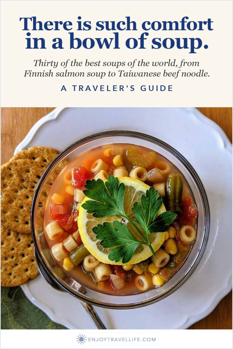 A bowl of minestrone with a lemon slice and crackers.