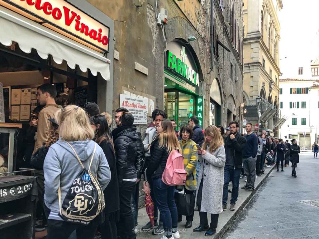 A line of locals and visitors stretches down the sidewalk outside All'Antico Vinaio in Florence, Italy.