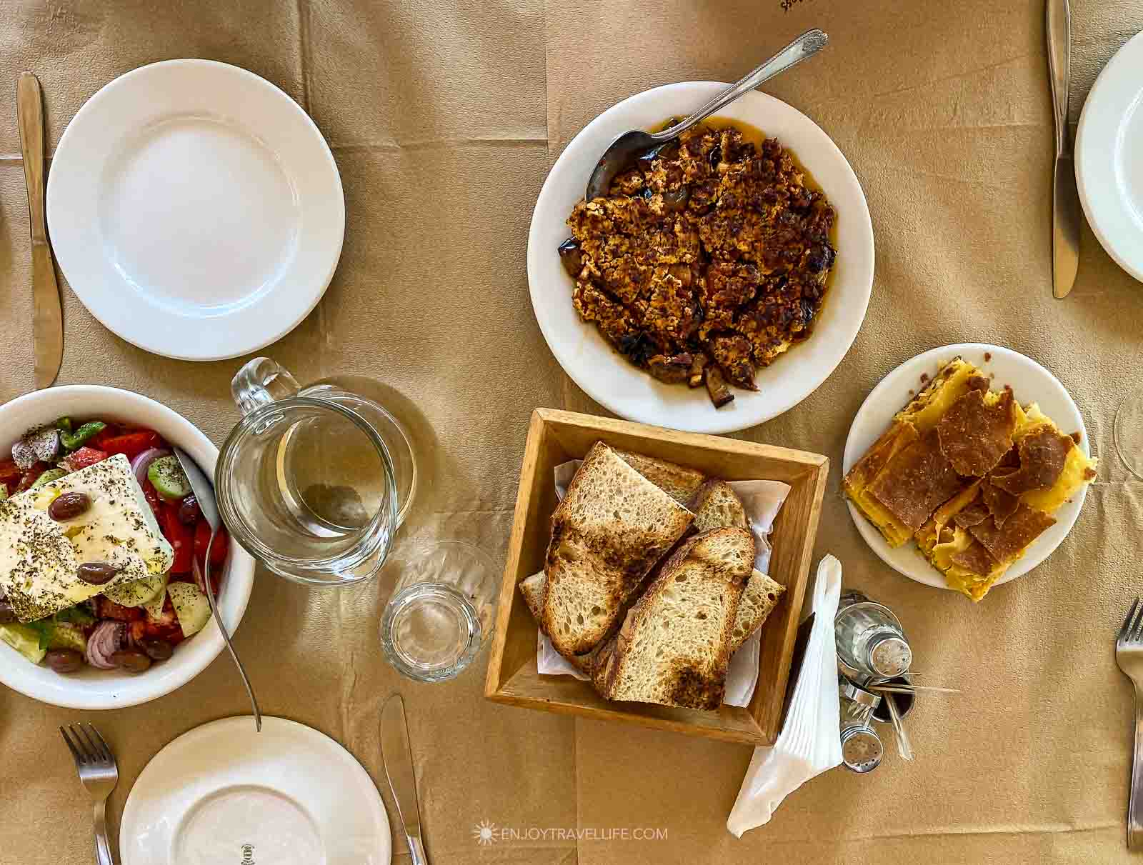 A table covered in kraft paper holds Greek salad, spinach pie, grilled bread, and small plates at the end of a food tour in Athens, Greece.