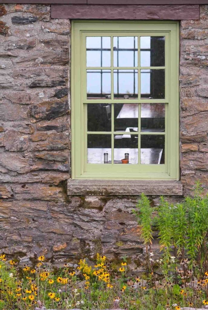A green-trimmed window in the stone wall of Bascom Lodge on Mount Greylock, with wildflowers below.