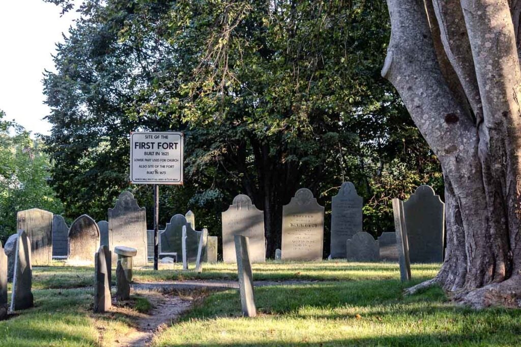 Old slate headstones surround a sign marking the site of the first fort on Burial Hill in Plymouth.