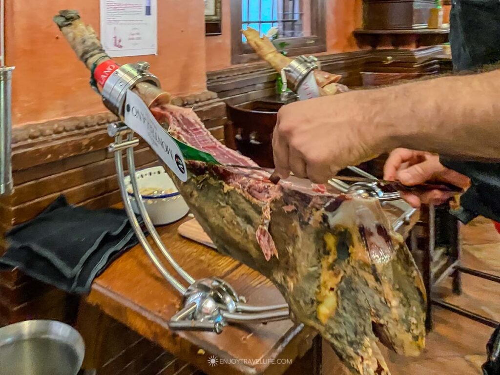 A shop worker in Granada, Spain, carves thin slices of jamon by hand from a leg clamped in a wooden stand.
