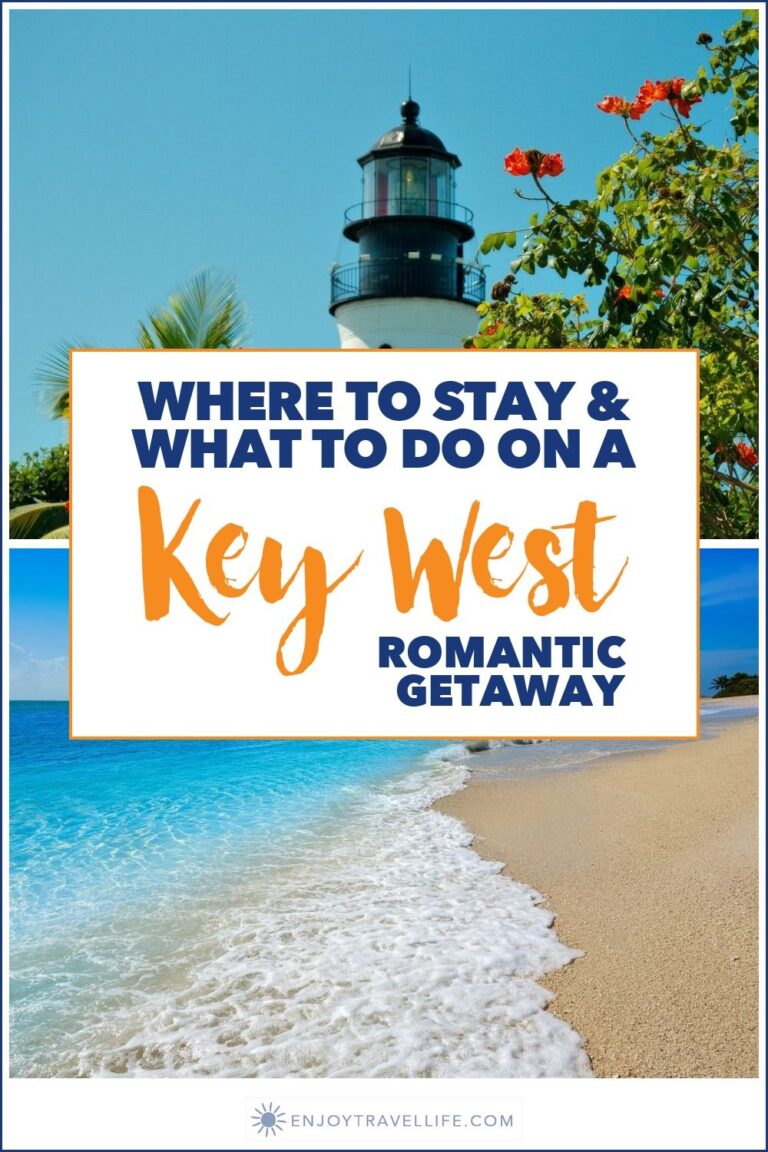 The Key West Lighthouse framed by palms and red blossoms above a white-sand beach and turquoise water, Key West, Florida.