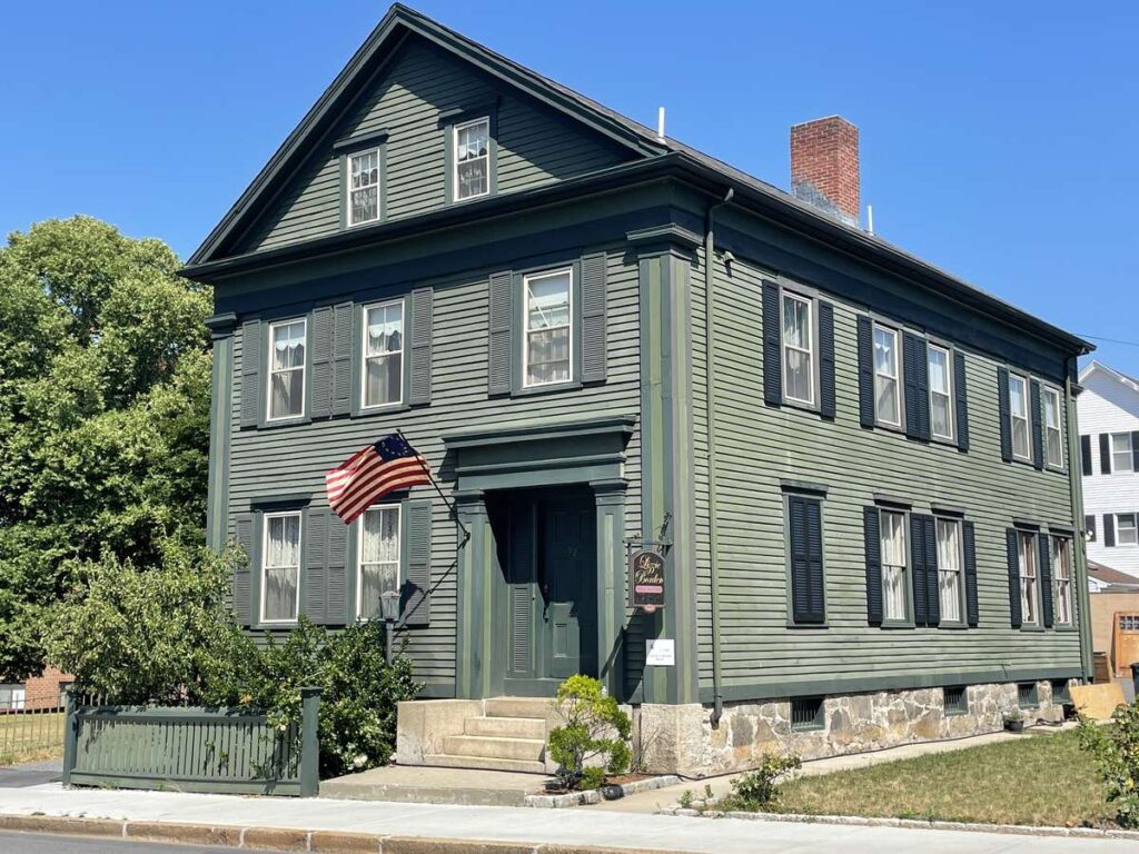 The Lizzie Borden House in Fall River is a green clapboard house with black shutters and an American flag by the front door.