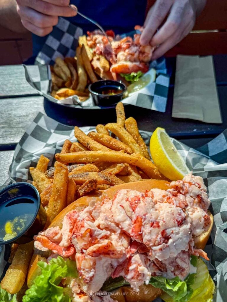 A lobster roll piled with chunks of fresh lobster sits in a paper-lined basket with fries and a lemon wedge in Onset on Cape Cod, Massachusetts.