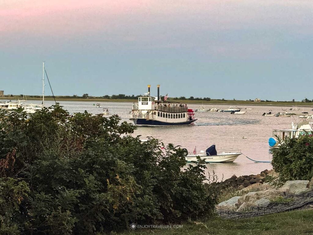 The Pilgrim Belle paddlewheel boat crosses Plymouth Bay at dusk, with passengers on its upper deck.