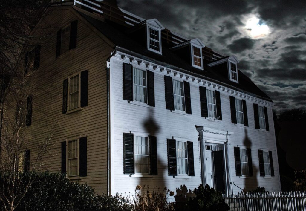 The white facade of the Ropes Mansion in Salem is lit at night under a cloudy, moonlit sky.