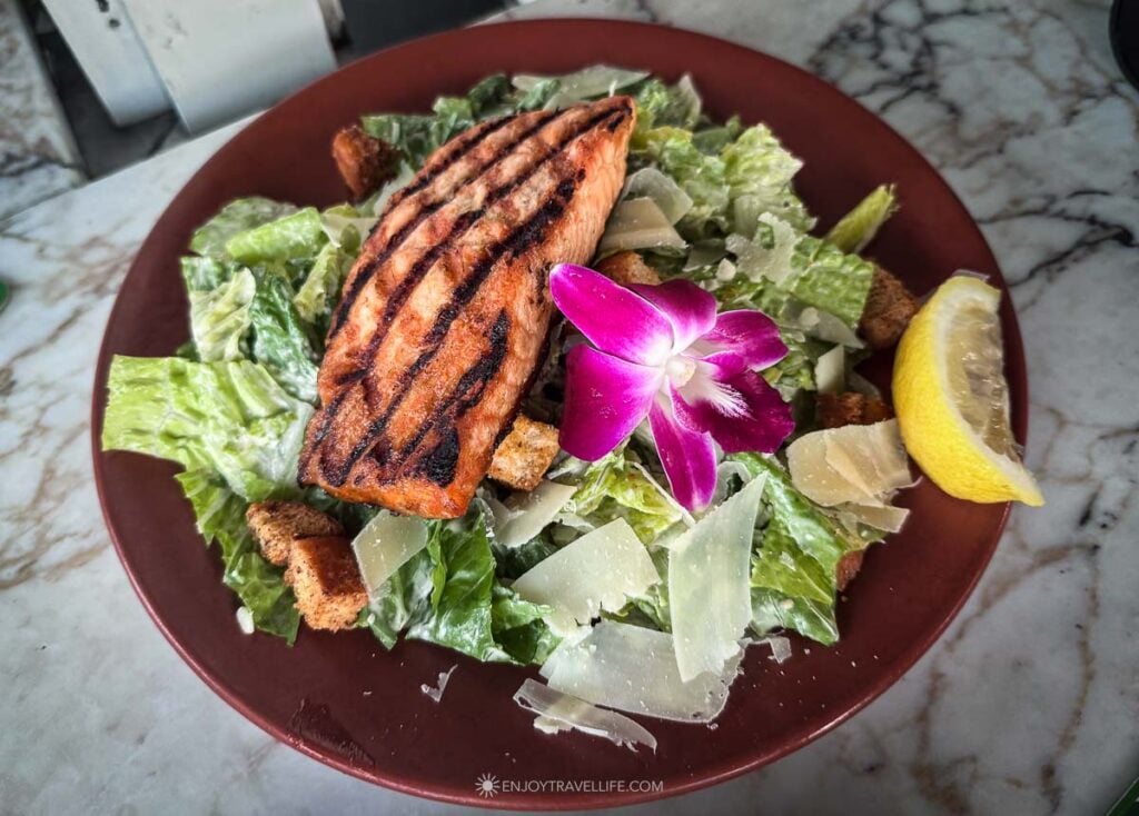 A grilled salmon Caesar salad garnished with an orchid and a lemon wedge is served at East Bay Grille in Plymouth.